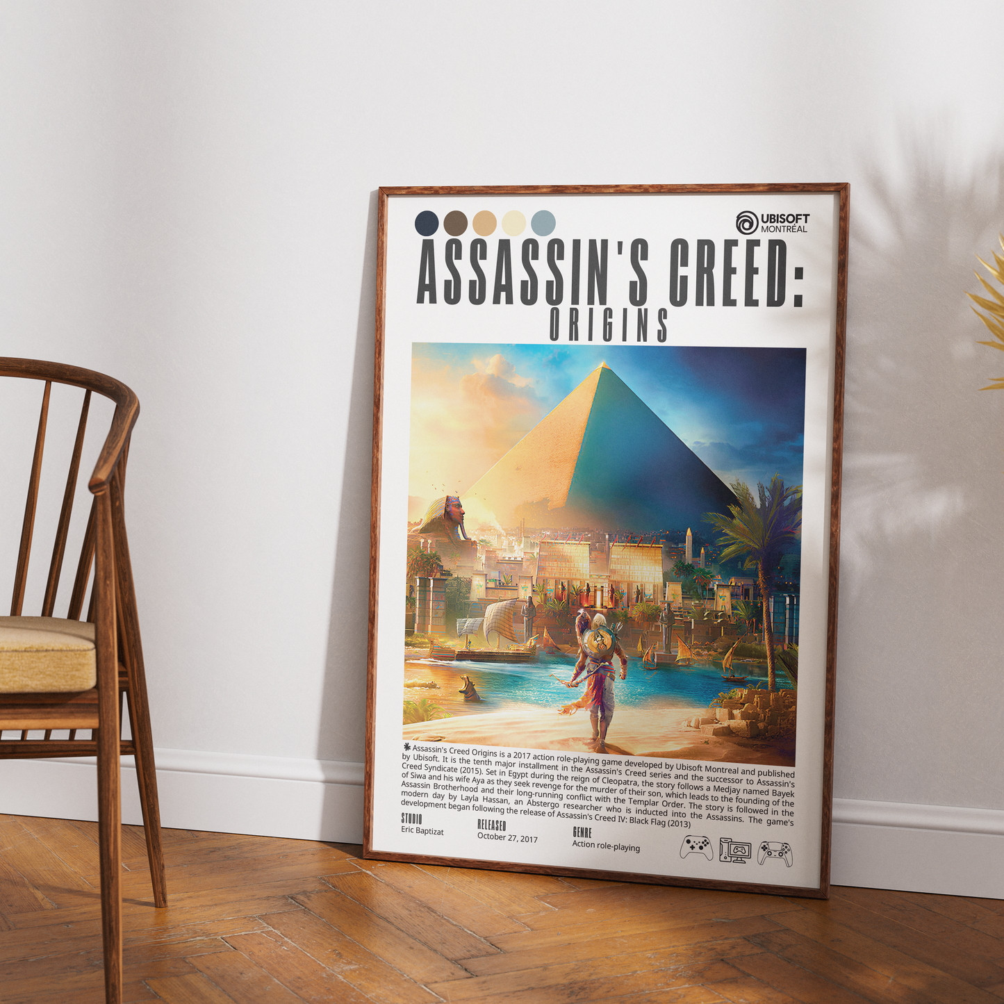 A framed Assassin's Creed: Origins poster leaning against a white wall on a wood floor, with part of a wooden chair visible on the left.