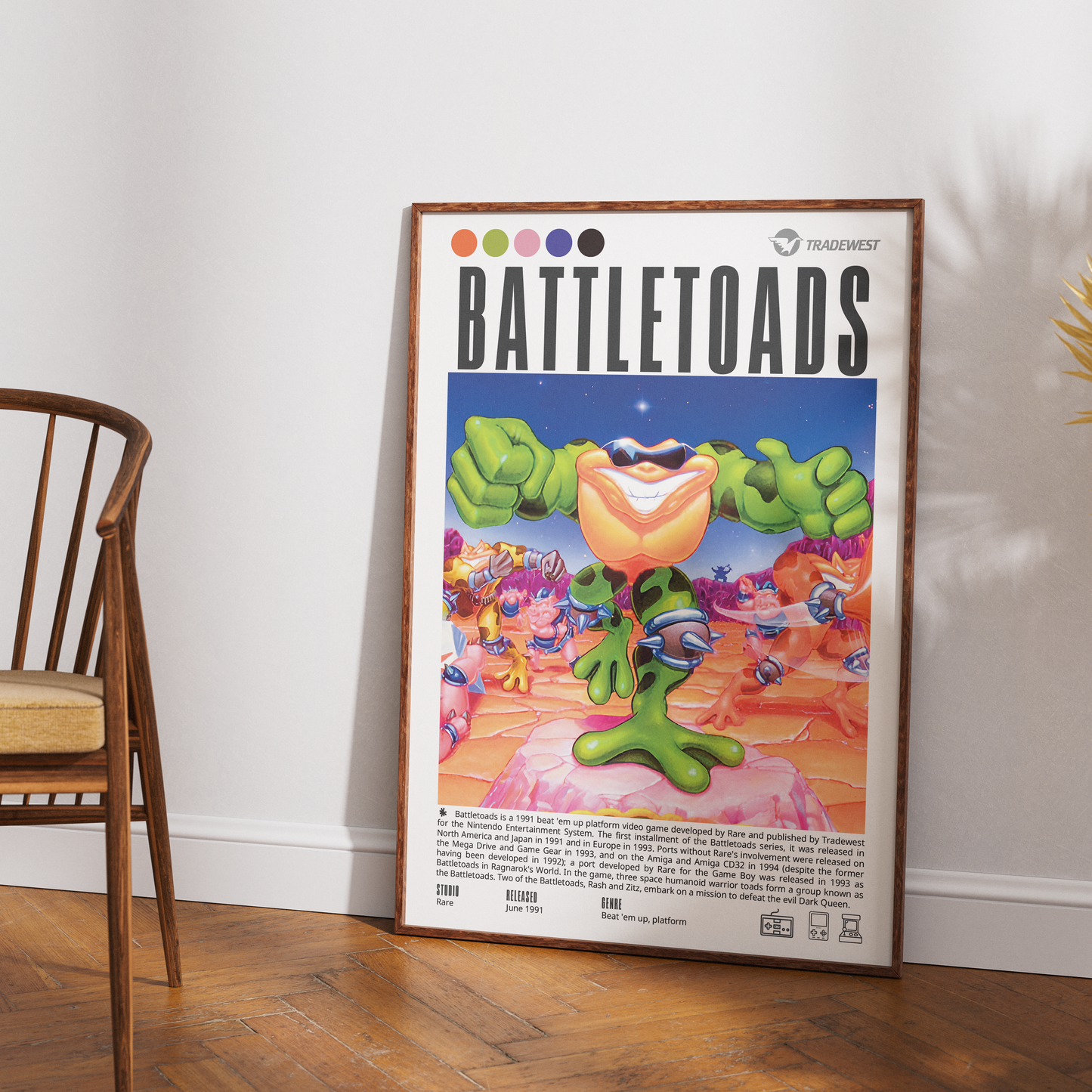 A framed Battletoads poster leaning against a white wall on a wooden floor, with part of a wooden chair visible on the left. The poster features colorful cartoon battletoads and the word Battletoads at the top.