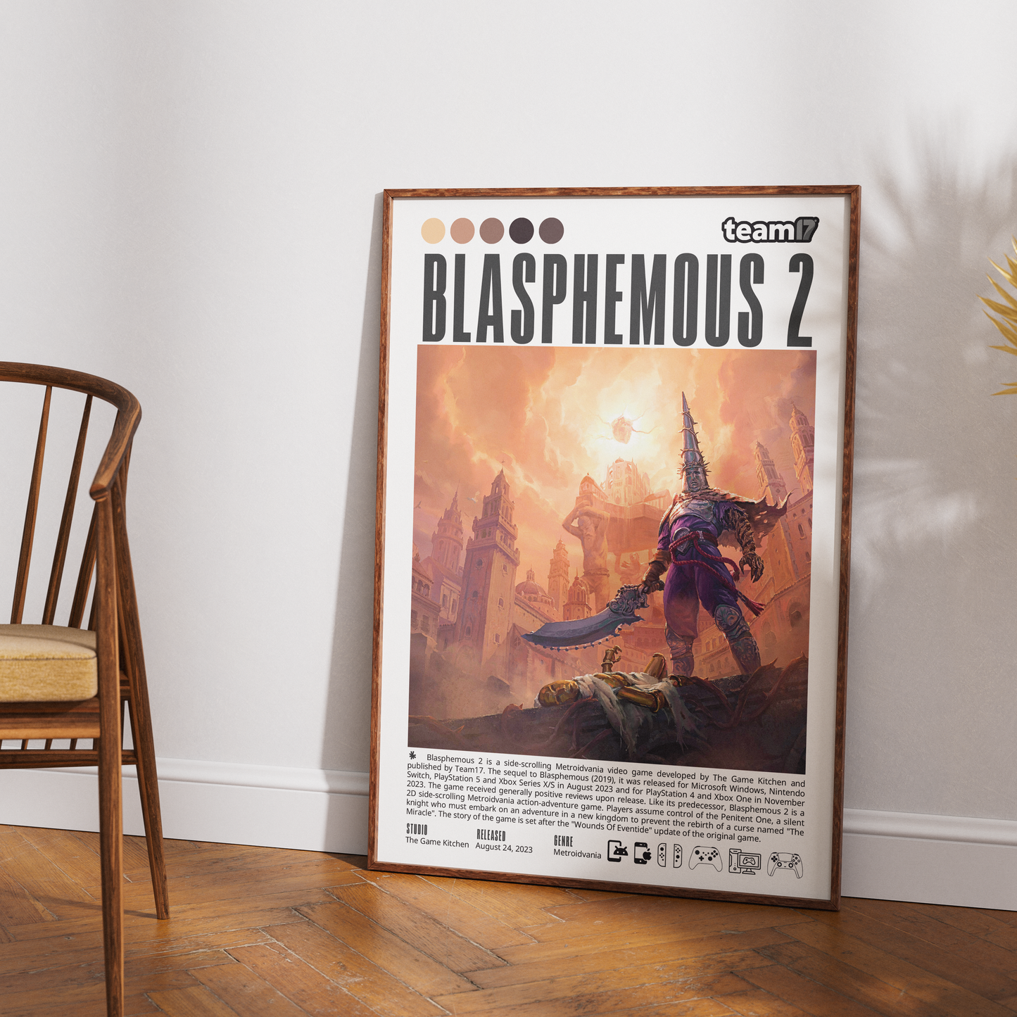 A framed Team 17 'Blasphemicus 2' poster is displayed leaning against a white wall on a wooden floor, next to a wooden chair.