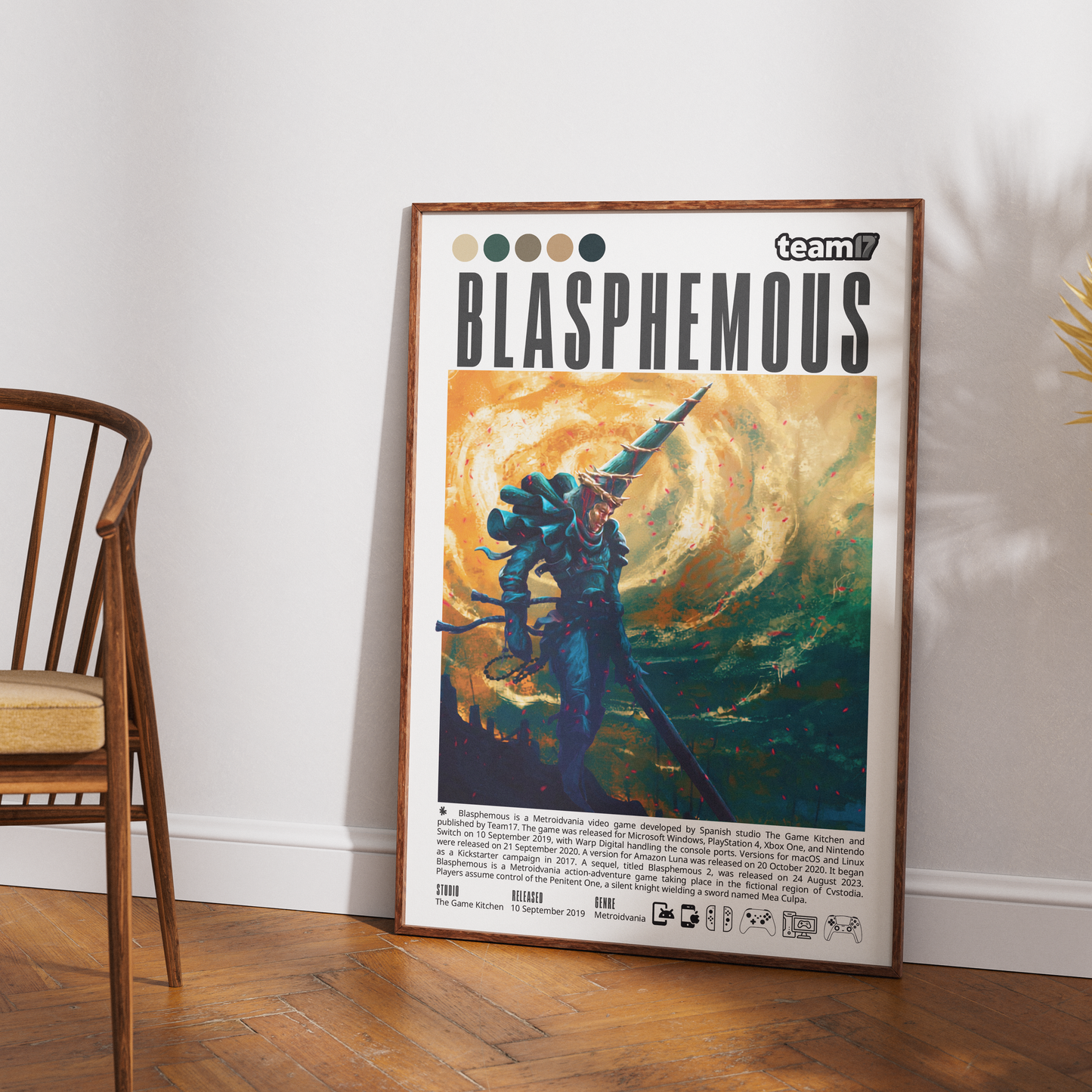A framed art poster titled 'BLASPHEMUS' with the 'team17' logo, leaning against a white wall on a wooden floor next to a wooden chair.