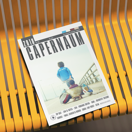 A magazine or booklet titled "2018 CAPERNAUM" lies on a yellow slatted bench. The cover shows a person in a blue shirt sitting on a skateboard outdoors near a railing, with small text along the bottom and a small logo at the lower left.