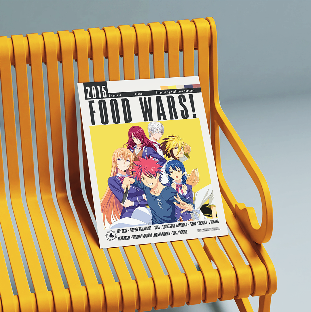 A printed magazine or book cover titled 'FOOD WARS!' with anime-style characters and a yellow cover, leaning on a bright yellow slatted bench against a soft gray studio background.