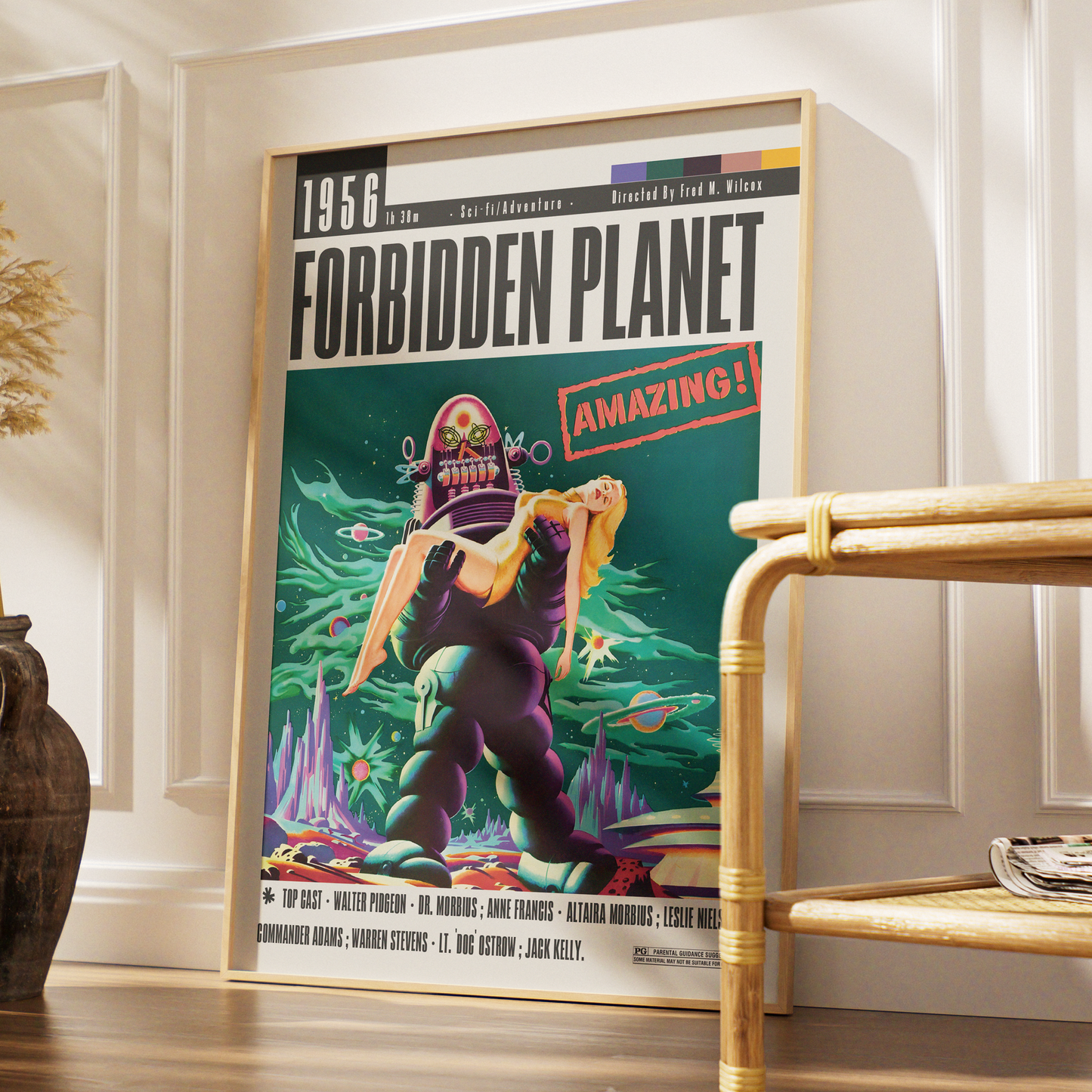 A framed vintage-style poster for the 1956 film 'Forbidden Planet' leaning against a white paneled wall in a styled interior setting with a bamboo side table and wooden floor.