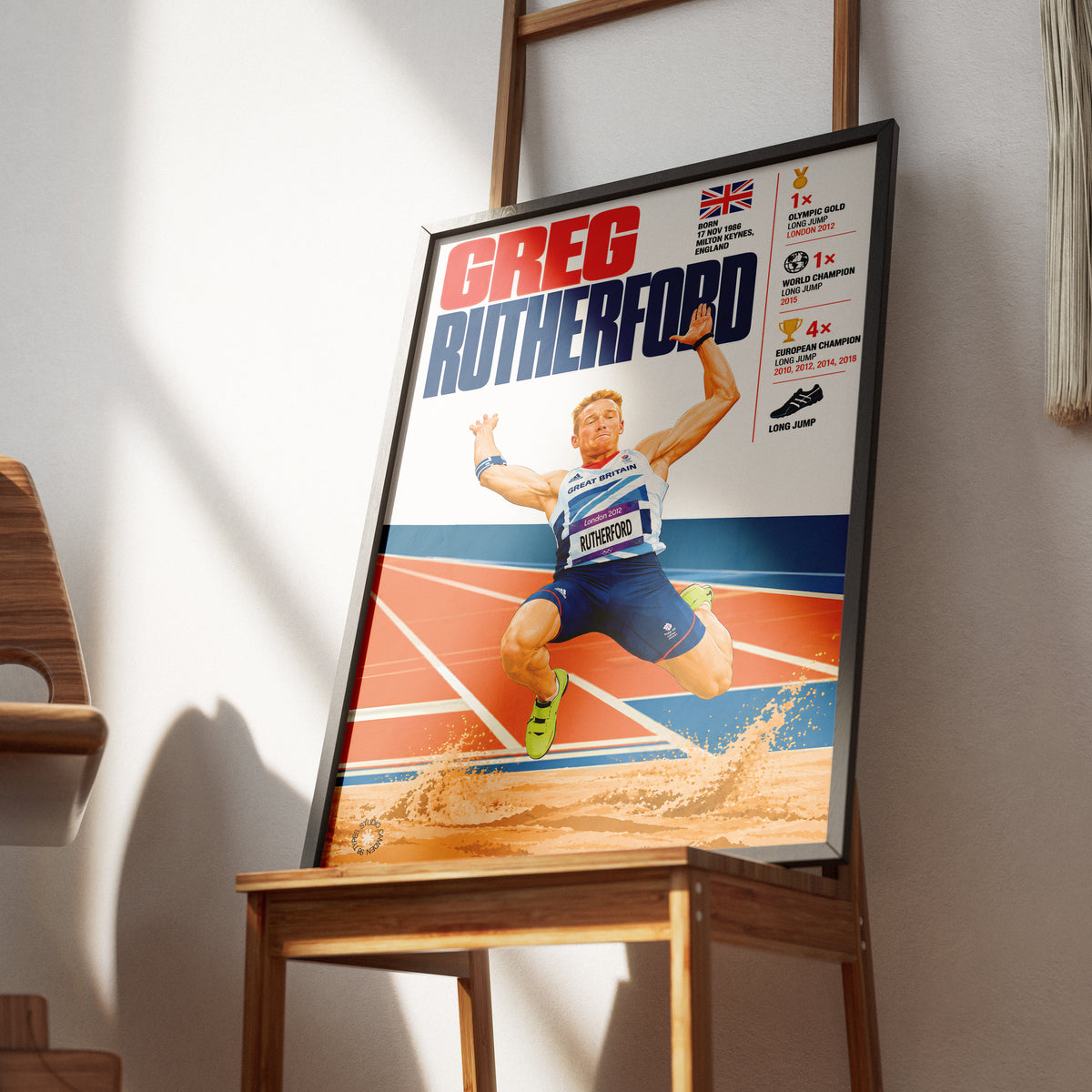 A framed sports poster of Greg Rutterford, an athlete in a blue and white uniform mid-jump on a track, leaning against a wall on a wooden table in a modern interior setting.