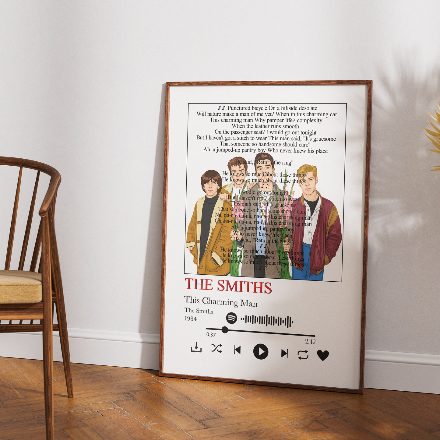 A framed music poster for The Smiths' 'This Charming Man' leaning against a white wall on a wooden floor, next to a wooden chair.