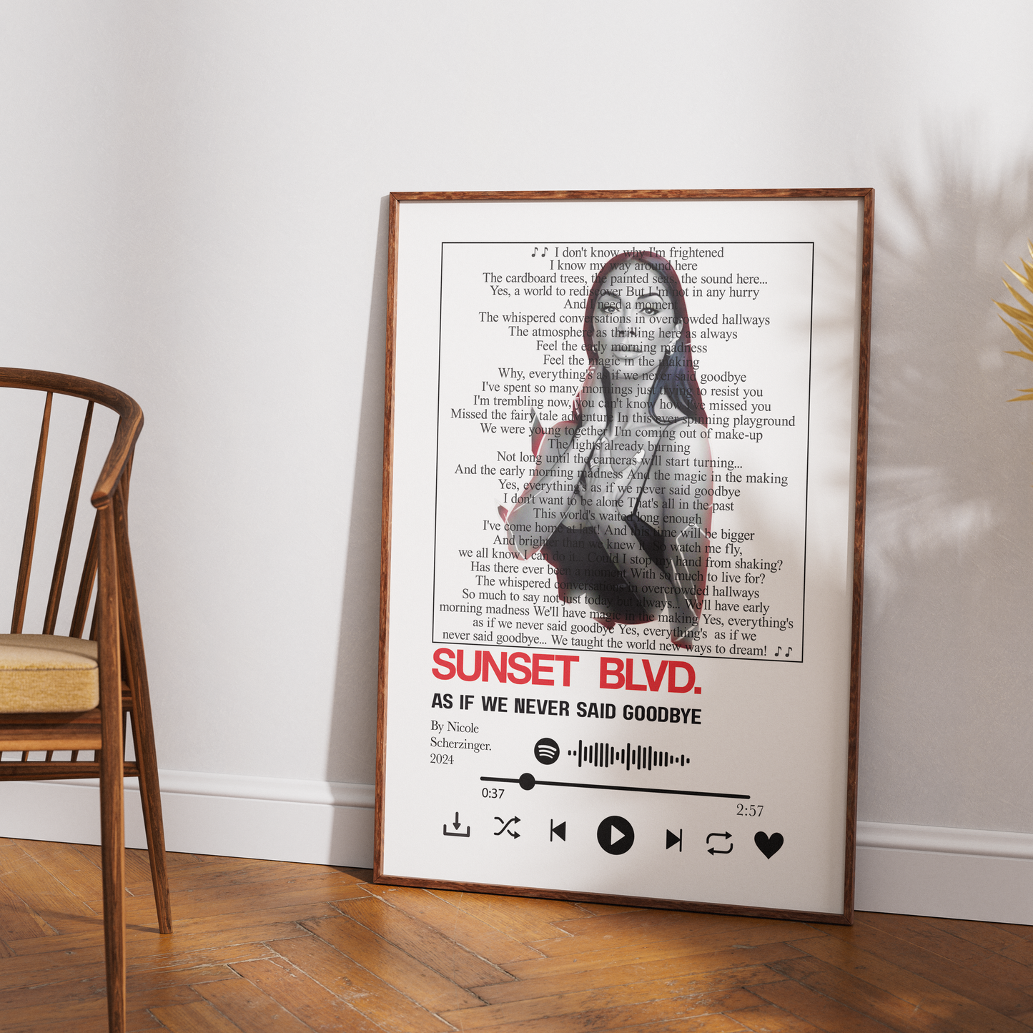 A framed music poster featuring the song 'As If We Never Said Goodbye' by Nicole Livermore, styled leaning against a white wall on a wooden floor next to a wooden chair.
