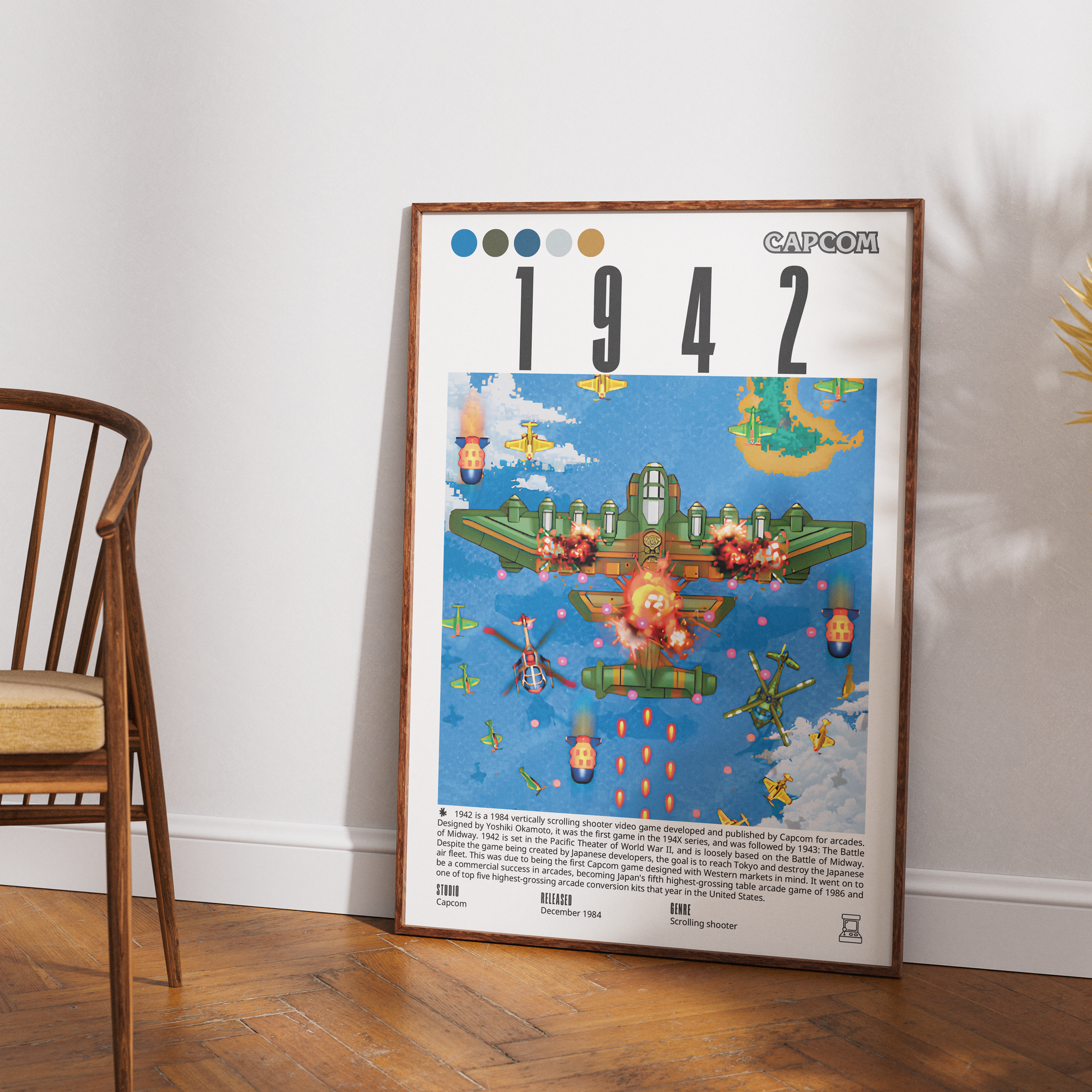 A framed Capcom 1942 poster leaning against a white wall on a wooden floor, next to a wooden chair.