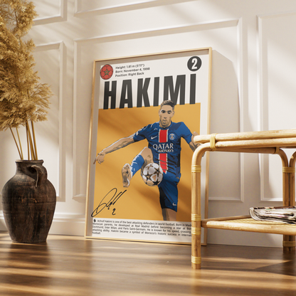 A framed soccer poster featuring a portrait of Neymar in a blue Paris Saint-Germain jersey with the name HAKIMI at the top, styled leaning against a white paneled wall on a wooden floor beside a rattan chair and a dark vase with dried grass.