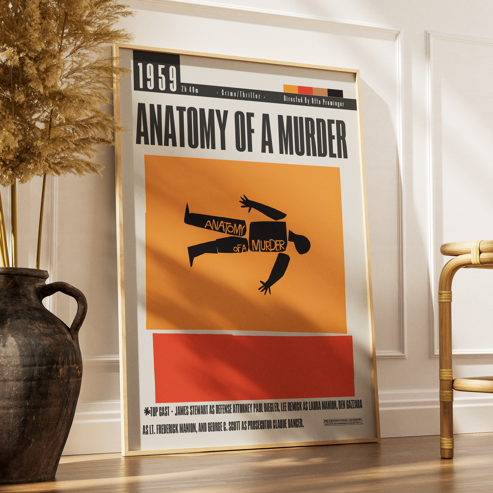 A framed vintage-style movie poster for the 1959 film 'Anatomy of a Murder' leaning against a white wall on a wooden floor, with a dark vase and part of a chair in the room.