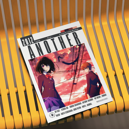 A magazine or book cover titled "ANOTHER 2012" lies on a yellow slatted chair. The cover features anime-style artwork with two characters against a pink and orange sky, with the text "Written and Directed by Toshiyuki Morikawa" visible.