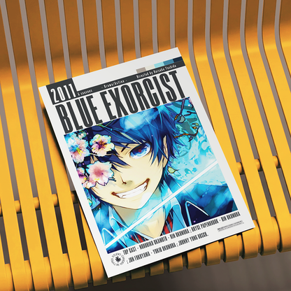A magazine or book titled "Blue Exorcist" lies diagonally on a yellow slatted bench. The cover features anime artwork of a blue-haired character with flowers and a bright blue watercolor background.