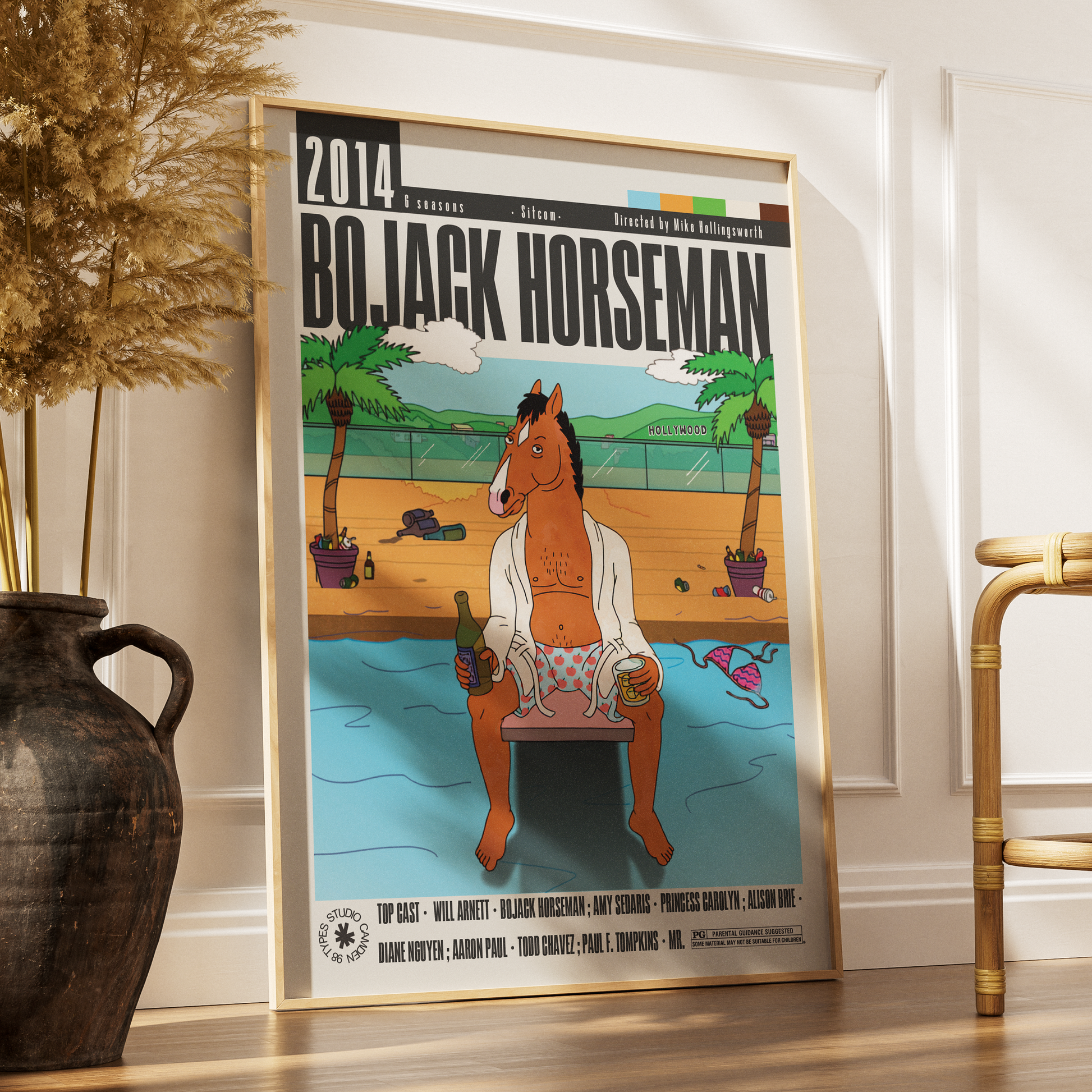 A framed 2014 BoJack Horseman movie poster leaning against a white wall on a wooden floor, styled in a home interior next to a dark ceramic vase with dried grass and a bamboo chair.