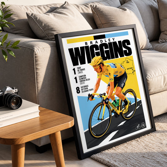 A framed cycling poster featuring Bradley Wiggins leaning against a beige sofa in a living room setting. The poster has a black frame, white mat, and a bold graphic design with yellow, blue, black, and white colors, showing Wiggins on a bicycle with text including 'BRADLEY WIGGINS' and stage numbers.