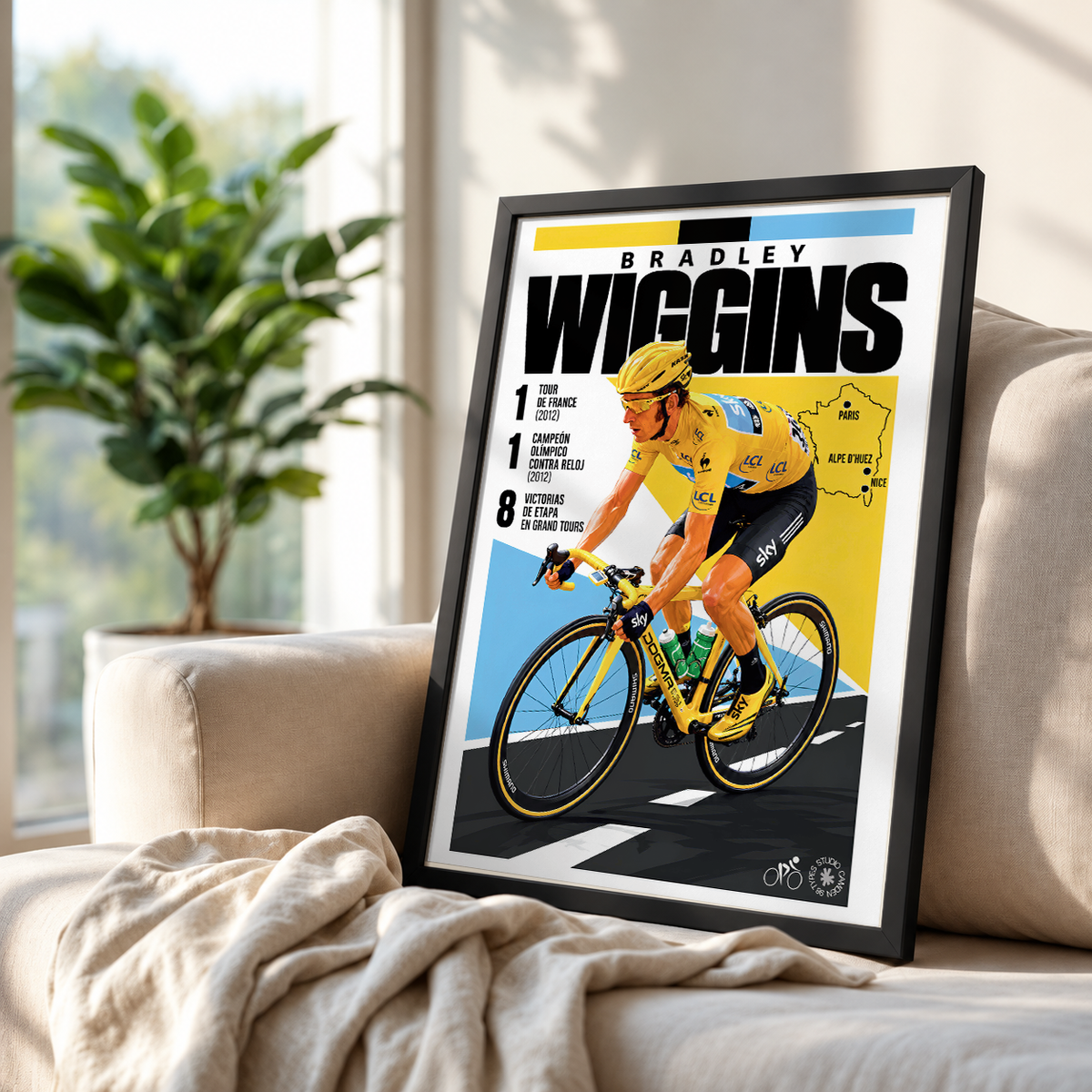 A framed cycling poster featuring Bradley Wiggins leaning against a beige sofa in a bright living room, with a plant and window in the background.