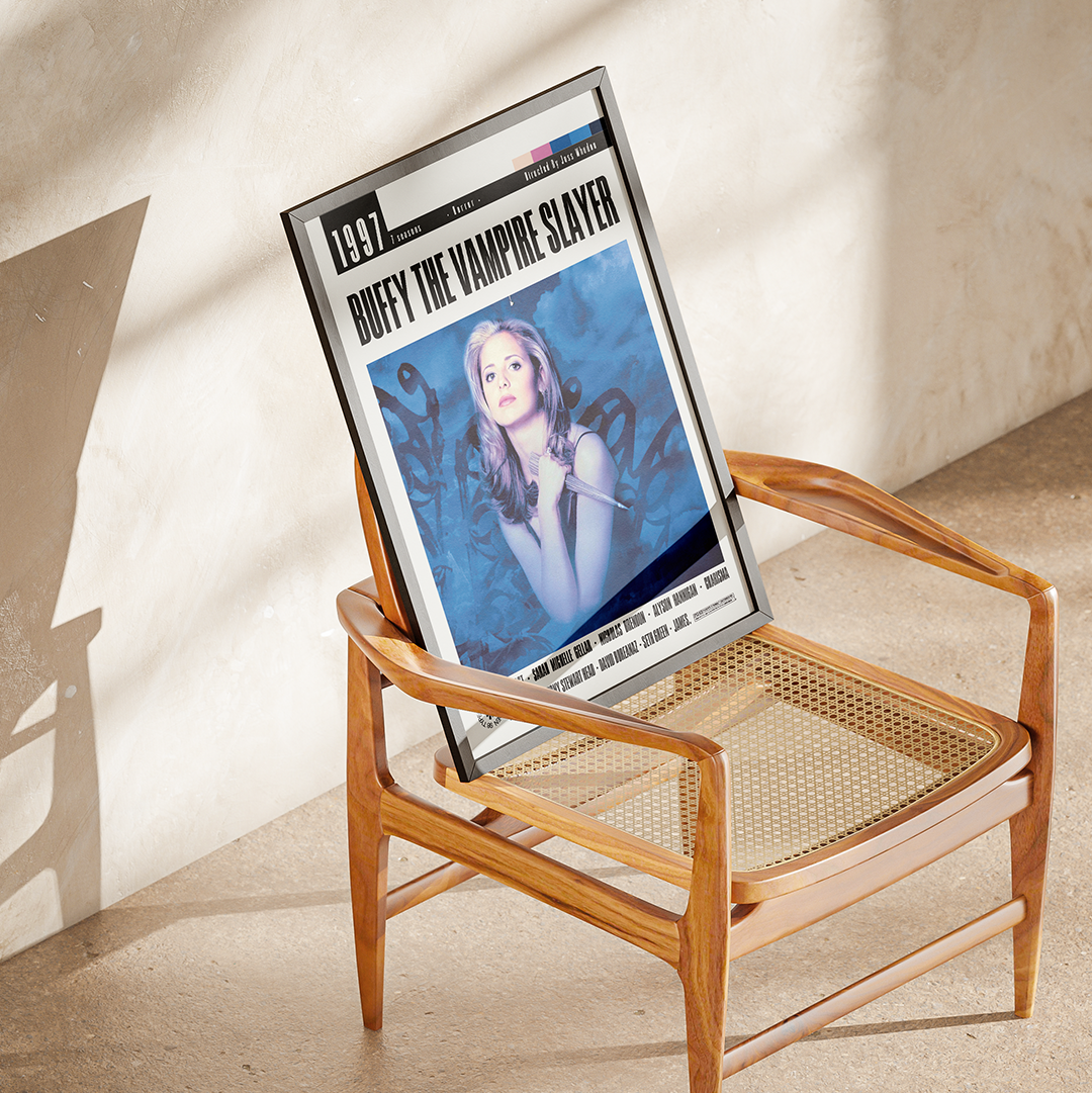 A framed art print featuring a cover design for 'Duffy the Vampire Slayer' leaning against a mid-century modern wooden armchair in a sunlit room.