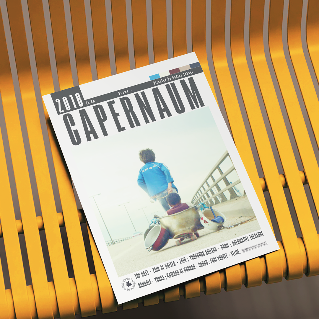 A magazine or booklet titled "2018 CAPERNAUM" lies on a yellow slatted bench. The cover shows a person in a blue shirt sitting on a skateboard outdoors near a railing, with small text along the bottom and a small logo at the lower left.