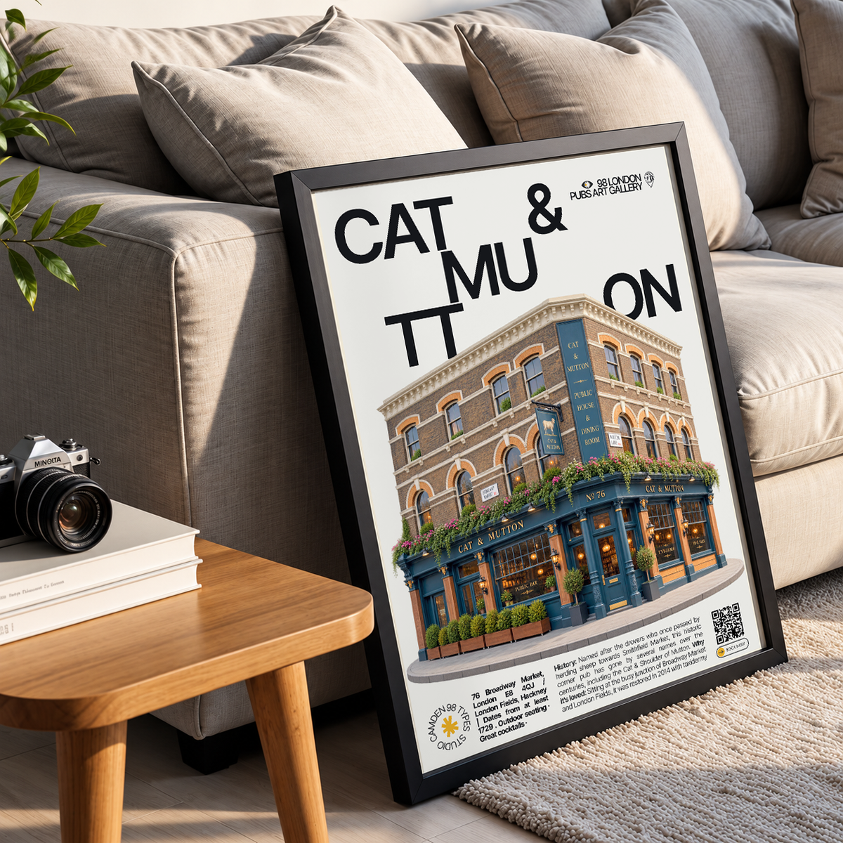 A framed poster leaning against a beige sofa in a living room setting. The poster features a black frame, bold black text reading 'CAT & MU ON', and an illustrated storefront scene with a brick building, blue awning, and greenery.