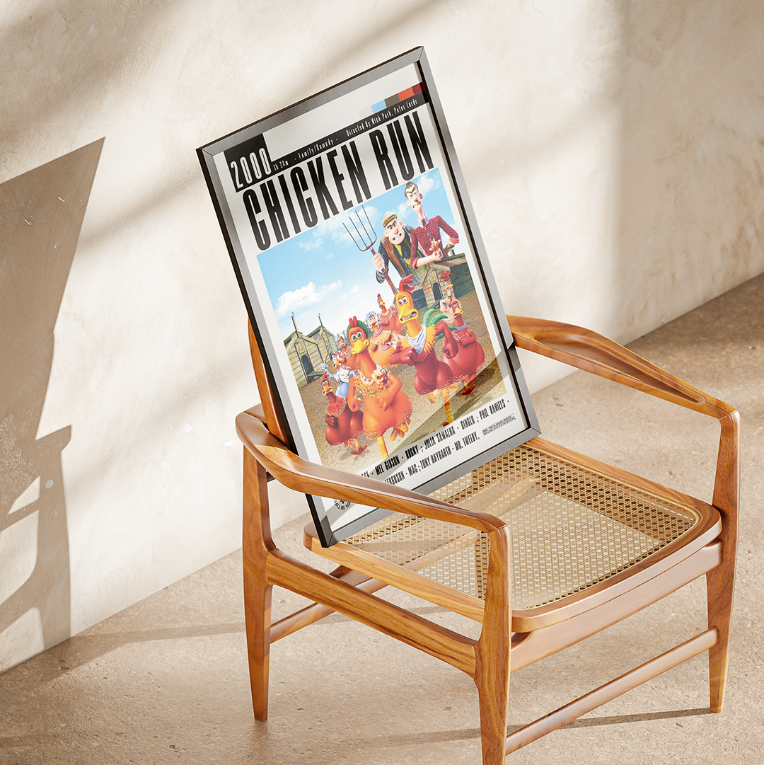 A framed '2001: Chicken Run' movie poster leaning against a wooden cane-seat chair in a sunlit room with a textured beige wall.