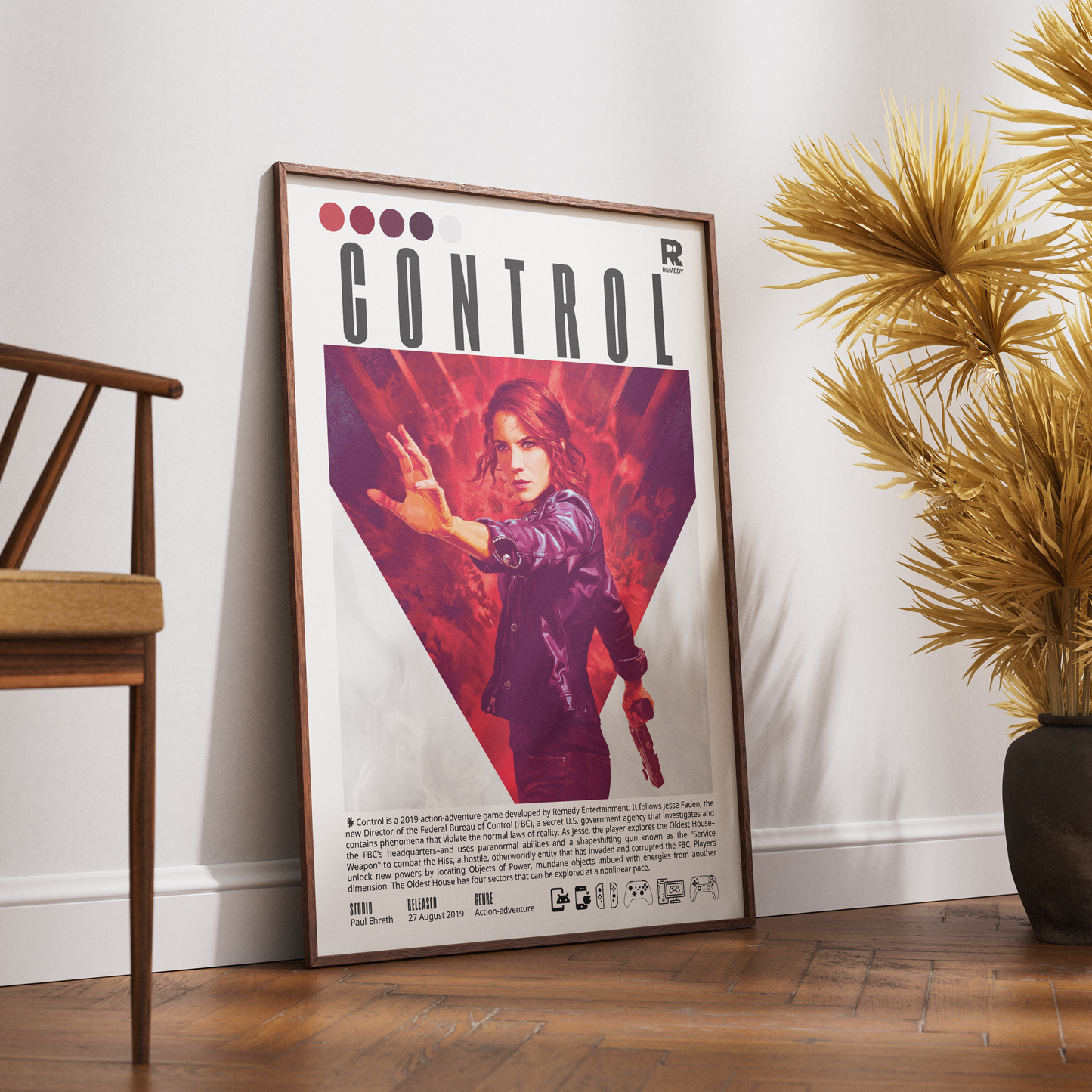 A framed poster of the video game Control leaning against a white wall on a wooden floor, styled with a wooden chair on the left and a potted plant on the right.