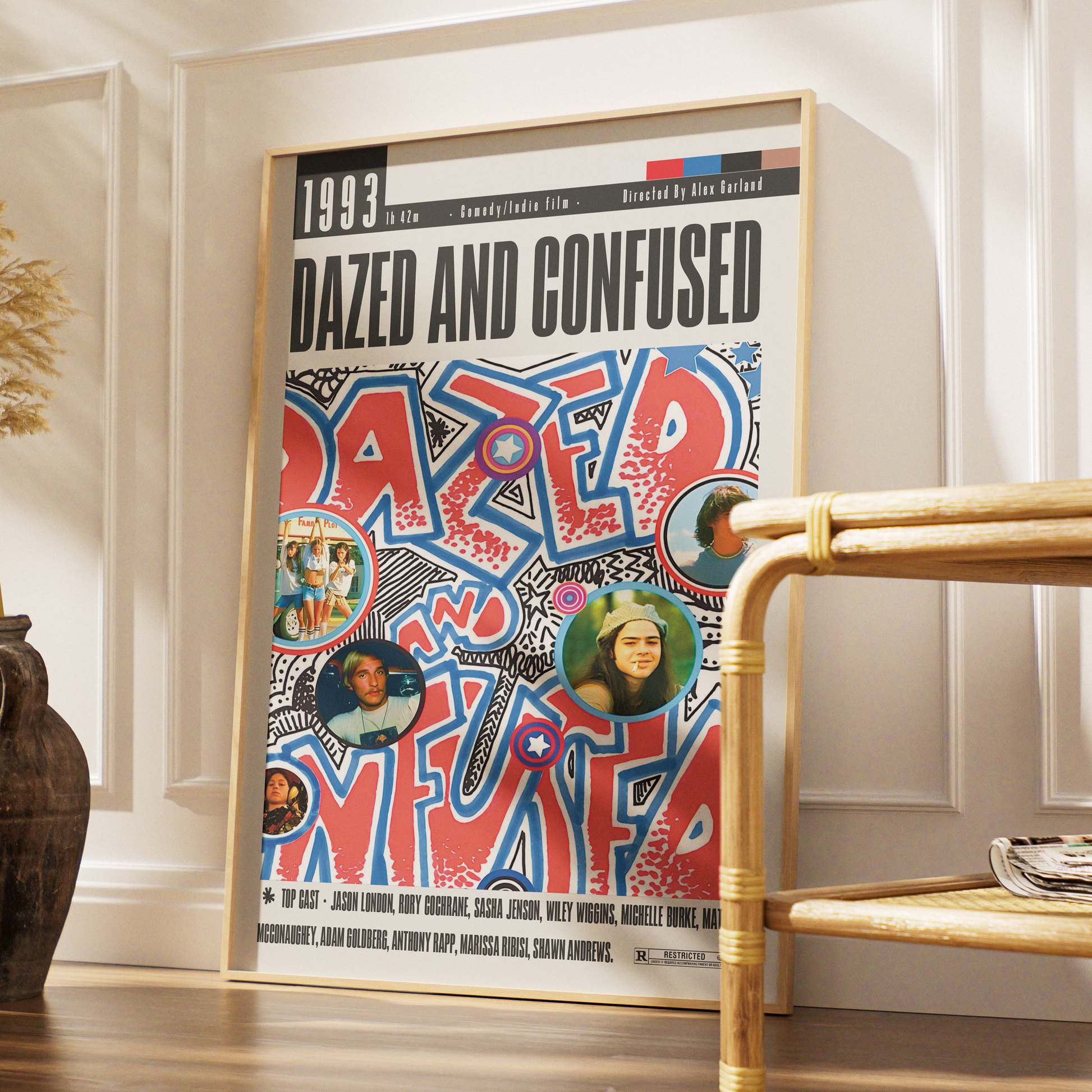 A framed poster of the movie 'Dazed and Confused' leaning against a white paneled wall in a styled interior setting with a bamboo side table and a dark vase.