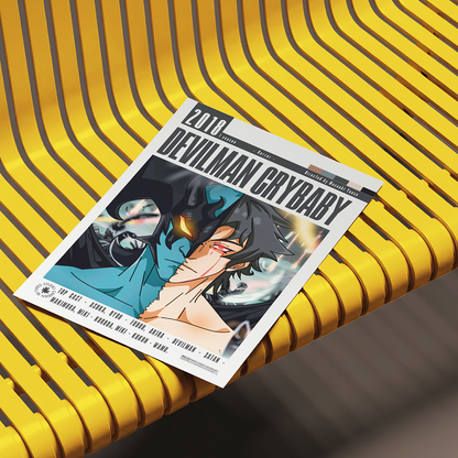 A printed magazine or album cover titled "2016 Devilman Crybaby" lies on a bright yellow ribbed bench. The cover features anime-style artwork with a dark-haired character in a teal top and black jacket, with track listing text along the bottom.