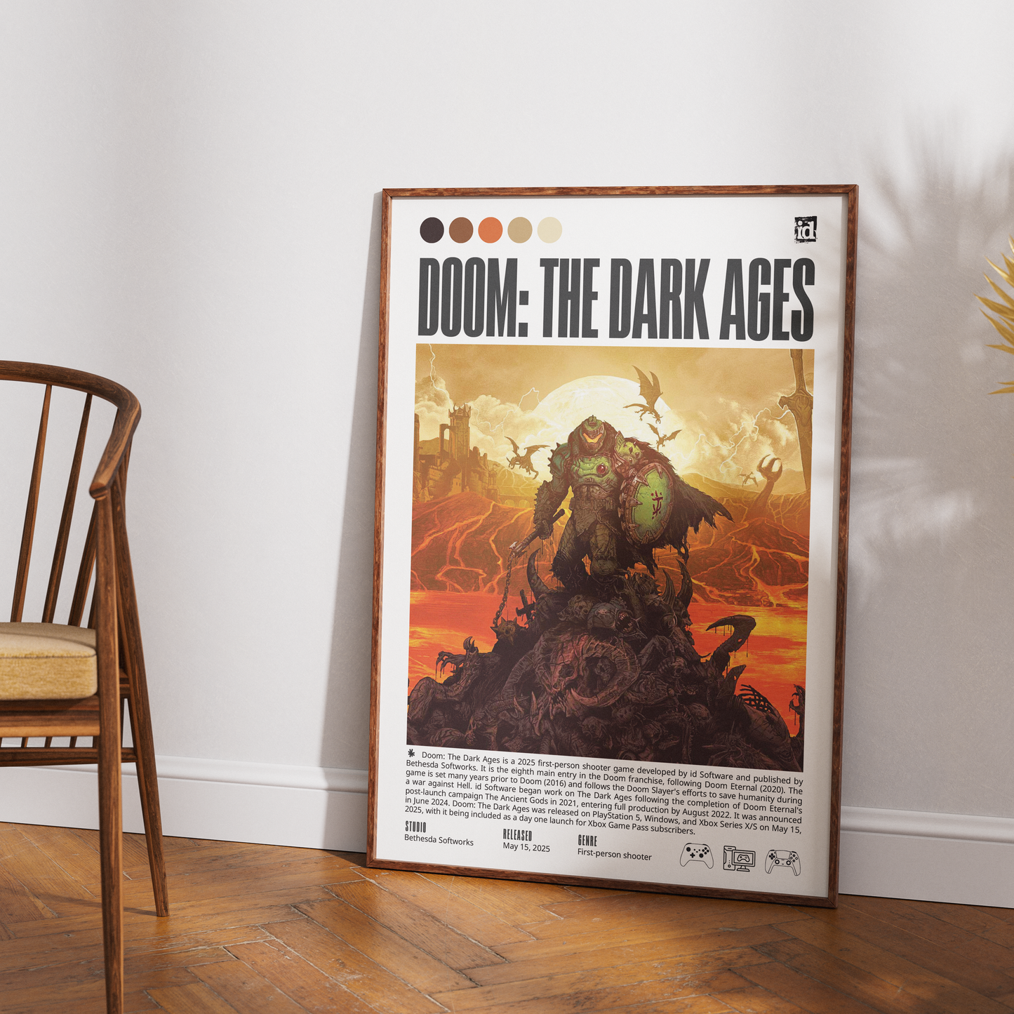 A framed vertical poster for the video game 'Doom: The Dark Ages' leaning against a white wall on a wooden floor, with part of a wooden chair visible on the left.