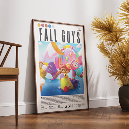 A framed 'Fall Guys' poster leaning against a white wall on a wooden floor, flanked by a wooden chair on the left and a potted palm on the right.