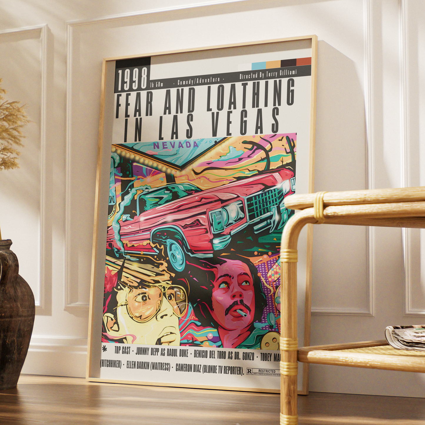 A framed pop-art poster leaning against a white paneled wall in a styled interior. The poster features bold text reading '1998 FEAR AND LOATHING IN LAS VEGAS' and a colorful illustration with a pink car, faces, and neon tones.