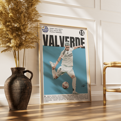A framed soccer poster featuring a player named Valverde, leaning against a white paneled wall on a wooden floor next to a dark vase with dried grass and a gold chair.