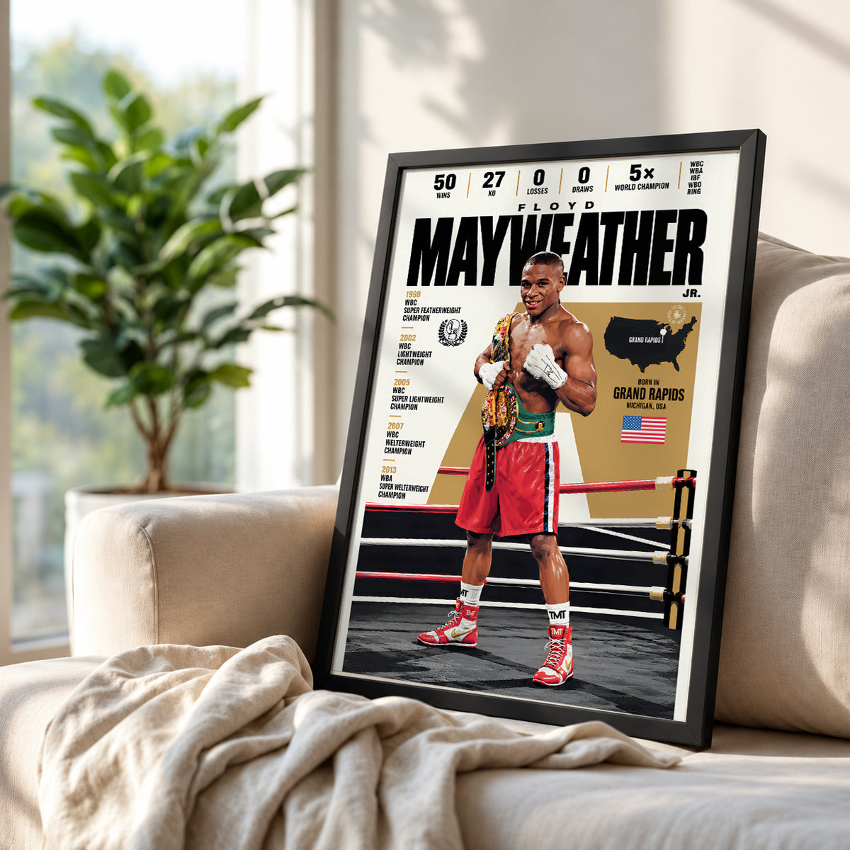 A framed boxing poster of Floyd Mayweather displayed on a beige sofa in a living room setting, with a blurred plant in the background.