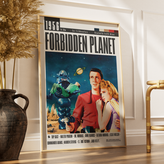 A framed vintage-style poster for the movie Forbidden Planet leaning against a white wall in a styled interior. The poster shows a man in a red uniform holding a woman next to a green robot, with a blue space background and the title 'FORBIDDEN PLANET' at the top.