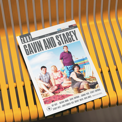 A printed movie poster for the 2007 film 'Gavin and Stacey' is displayed at an angle on a yellow slatted bench. The poster features the cast members sitting and standing on a beach, with the title 'GAVIN AND STAGEY' in large black letters at the top.