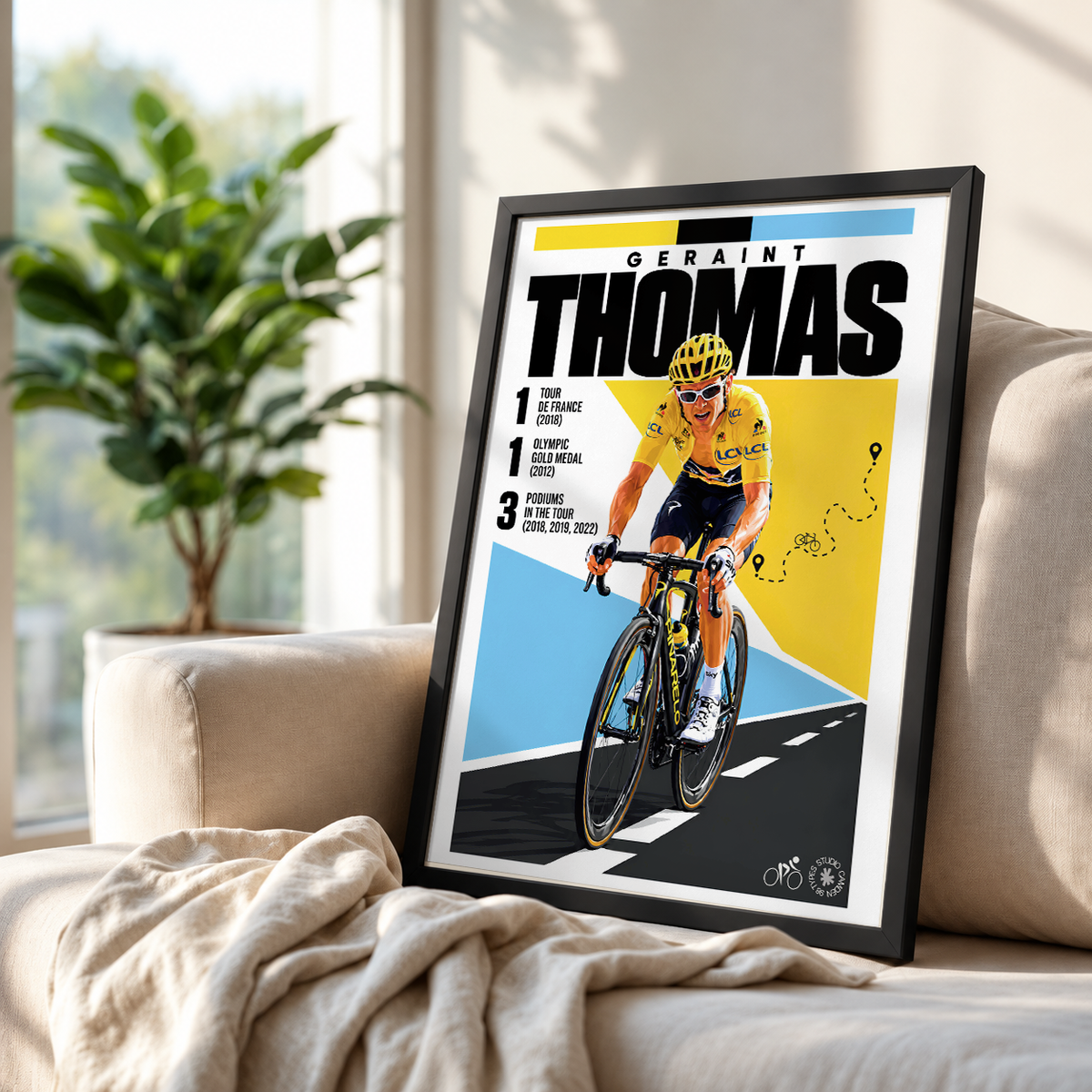 A framed cycling poster leaning against a beige sofa in a bright room, with a potted plant in the background. The poster features Geraint Thomas on a road bike with bold black, yellow, and blue graphic design and the text 'GERAINT THOMAS'.