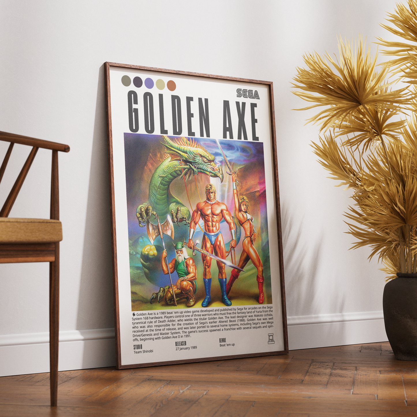 A framed retro-style 'Golden Axe' poster leaning against a white wall on a wooden floor, with a wooden chair on the left and a potted palm on the right.