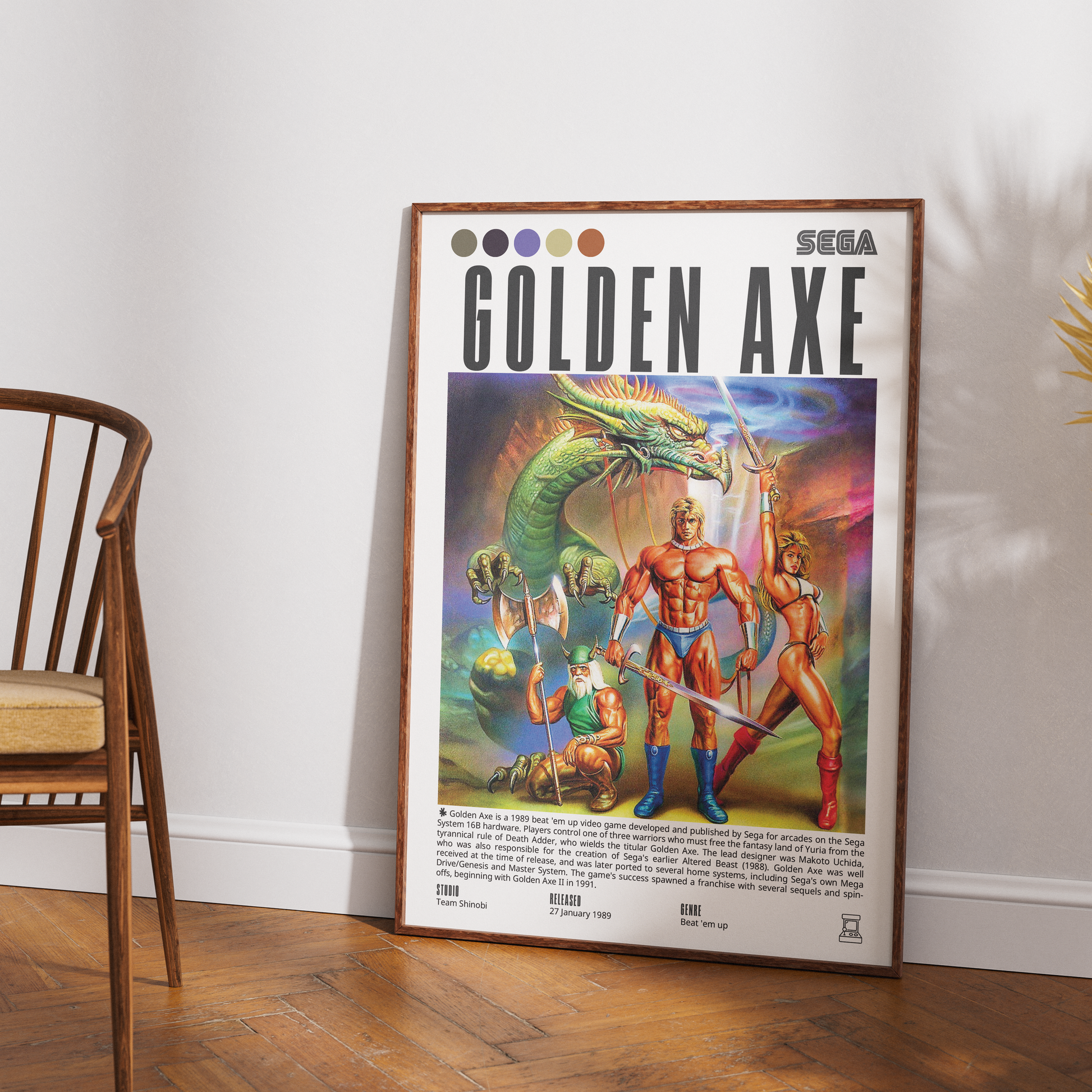 A framed vintage-style 'Golden Axe' Sega poster leaning against a white wall on a wood floor, with part of a wooden chair visible on the left.