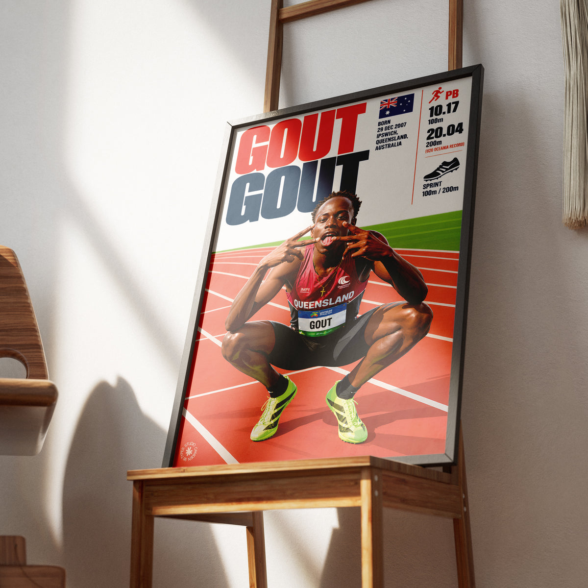A framed sports poster of sprinter Gout leaning against a wooden chair in a modern room with warm sunlight and shadows.