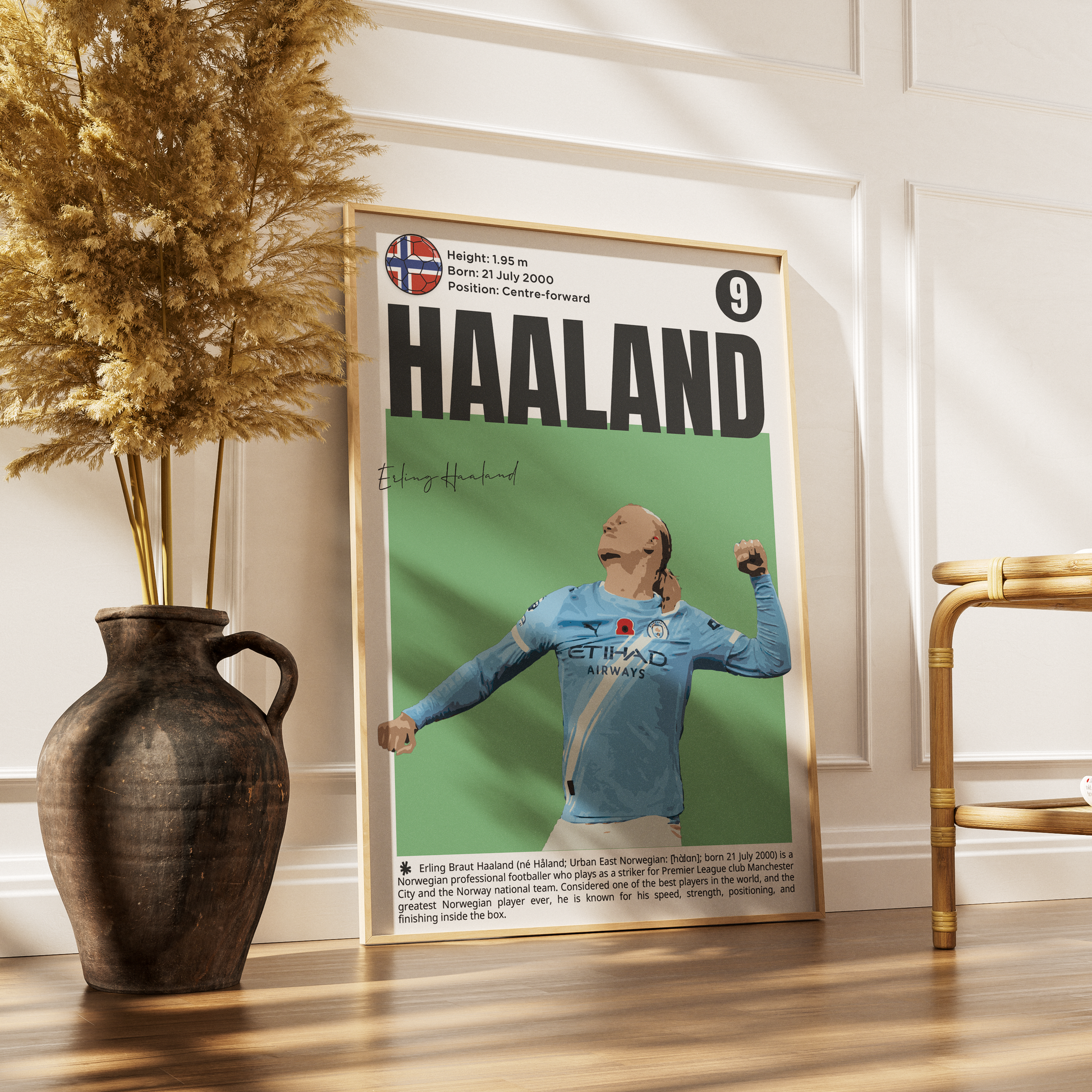 A framed sports poster of cyclist Jumbo Haaland leaning against a white paneled wall on a wooden floor, styled with a dark ceramic vase of dried grass on the left and a gold chair on the right.