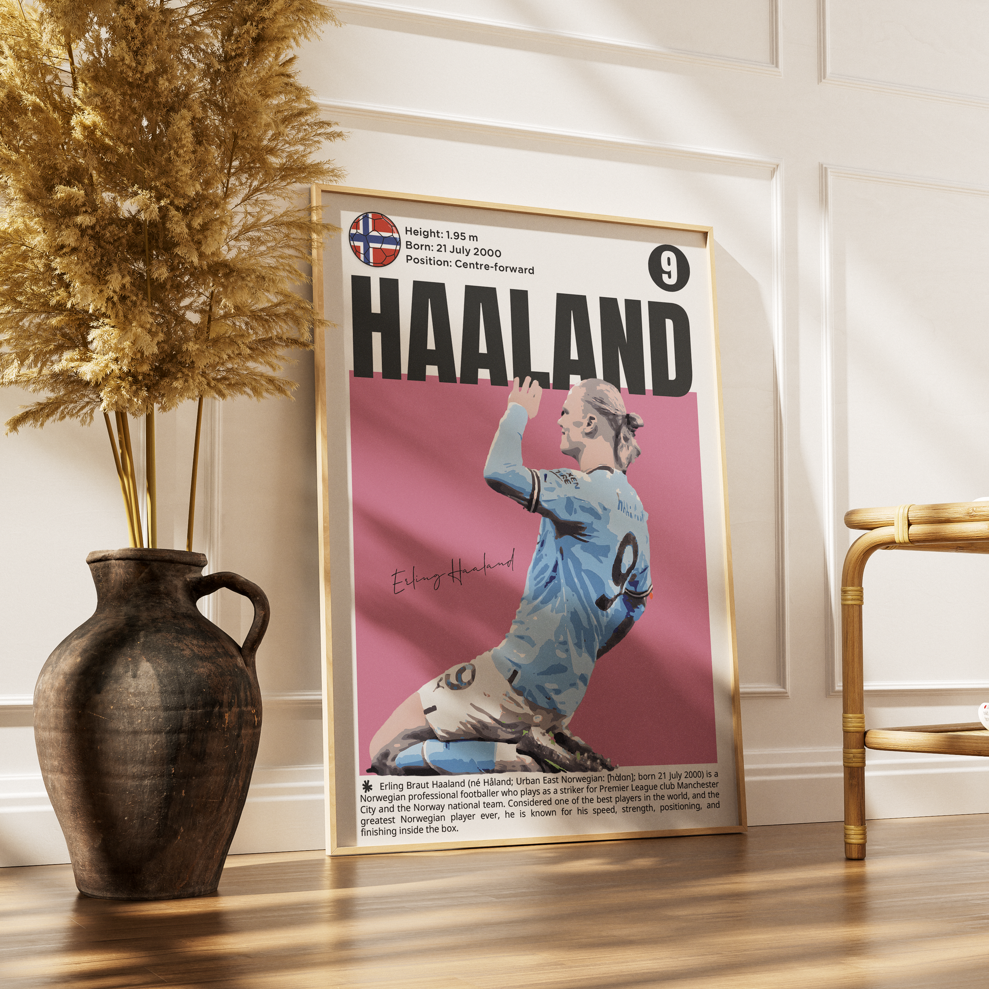 A framed poster of soccer legend Peter Haaland, styled in a modern room setting leaning against a white paneled wall on a wooden floor, next to a rustic vase with dried grass and a gold chair.