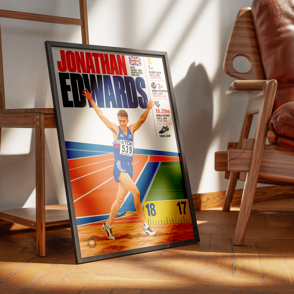 A framed sports poster of athlete Jonathan Edwards leaning against a wall in a modern wooden room setting.