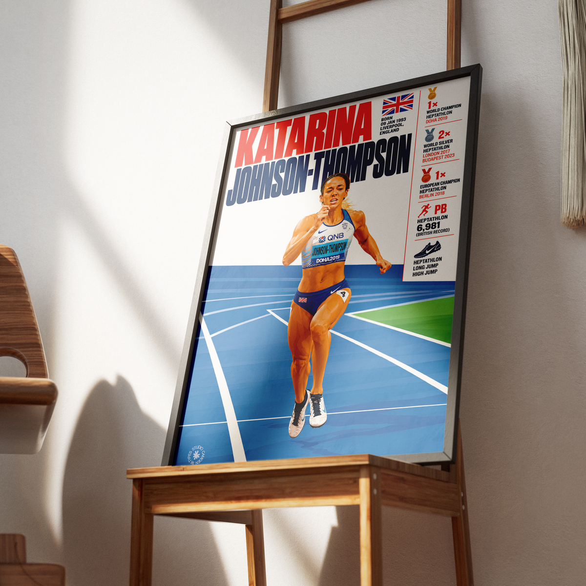 A framed sports poster of Katarina Johnson-Thompson, an Australian track and field athlete, leaning on a wooden table in a modern room with warm natural light.