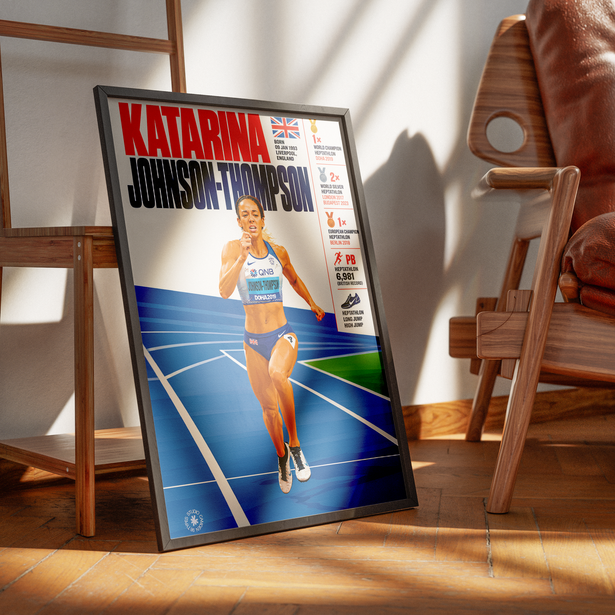 A framed sports poster leaning against a wall on a wooden floor, showing athlete Katarina Johnson-Thompson on a blue track. The poster is displayed in a warm, modern room setting with wooden chairs and strong sunlight casting shadows.