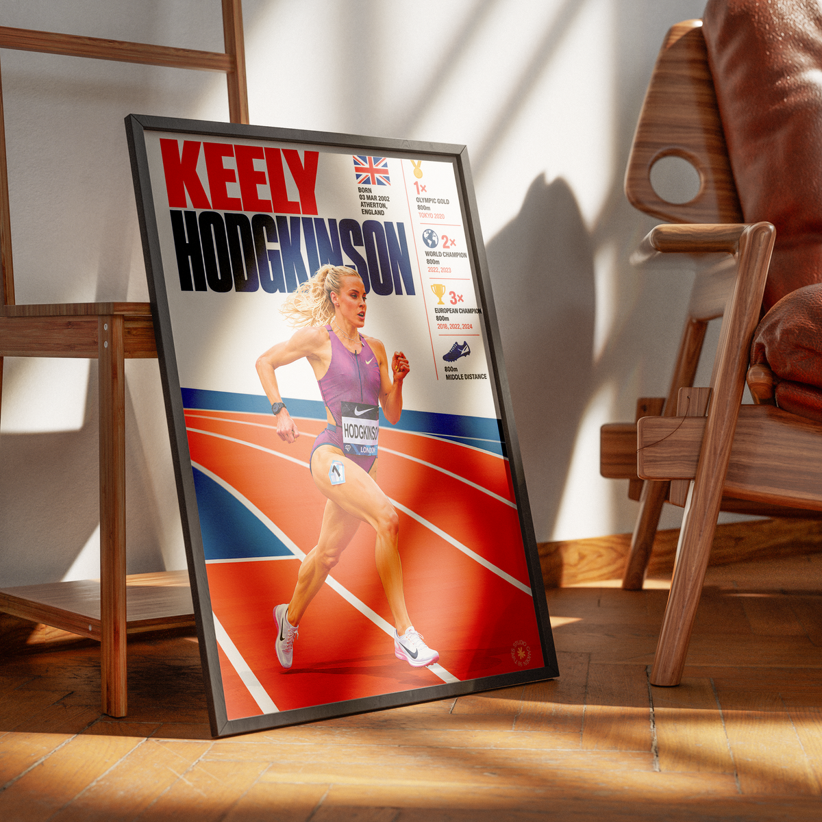 A framed sports poster of Keely Hodgkinson leaning against a wall on a wooden floor, styled in a modern room with wooden chairs and warm sunlight.