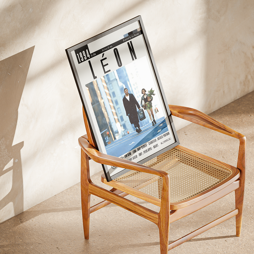 A framed magazine or poster print featuring the cover story 'LÉON' from 1991, displayed on a mid-century modern wooden armchair with woven cane seats in a sunlit room.