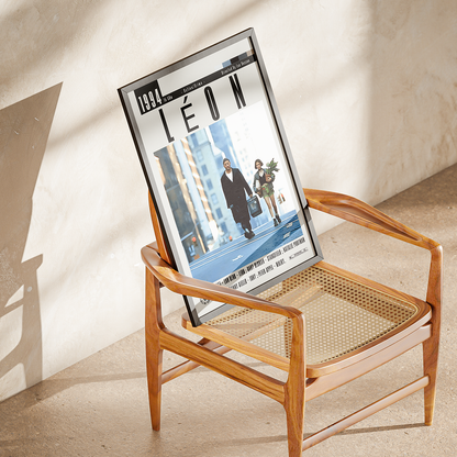 A framed magazine or poster print featuring the cover story 'LÉON' from 1991, displayed on a mid-century modern wooden armchair with woven cane seats in a sunlit room.