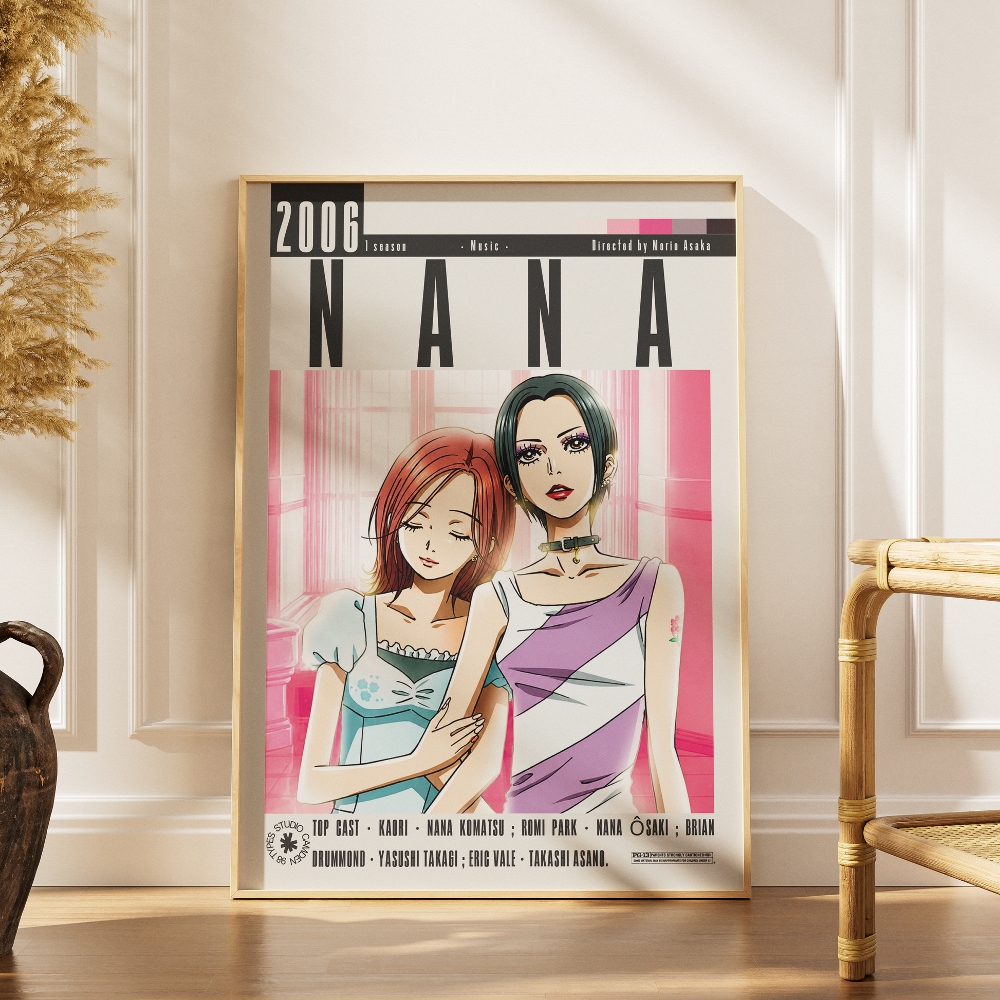 A framed anime poster of Nana from the movie '2006' leaning against a white paneled wall on a wooden floor, with a bamboo chair and dried grass in the background.