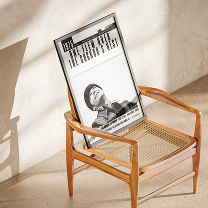 A framed black-and-white poster leaning against a wooden armchair in a sunlit room with a textured beige wall and floor.