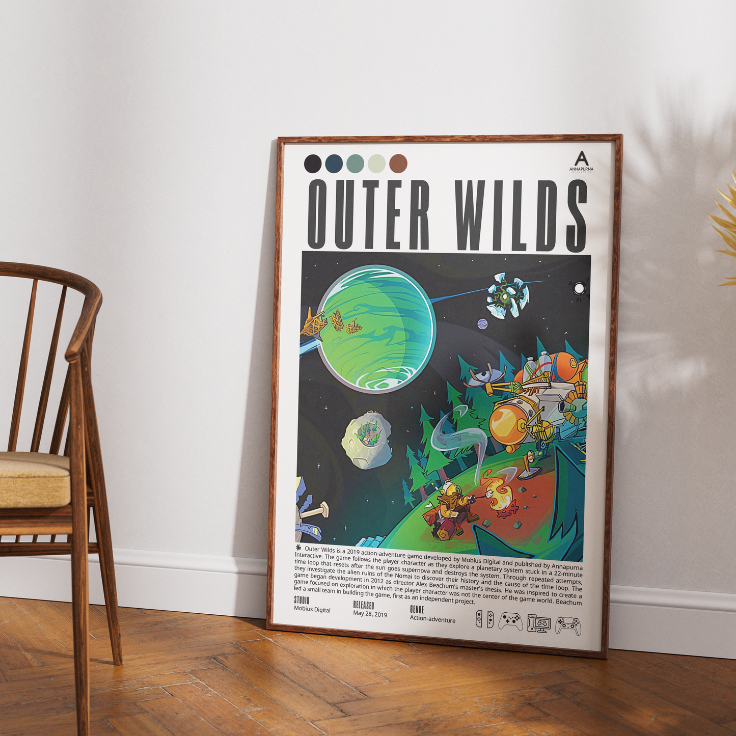A framed art print titled 'OUTER WILDS' leaning against a white wall on a wooden floor, next to a wooden chair. The poster features a colorful retro-futuristic space illustration with planets, aliens, and a spaceship.