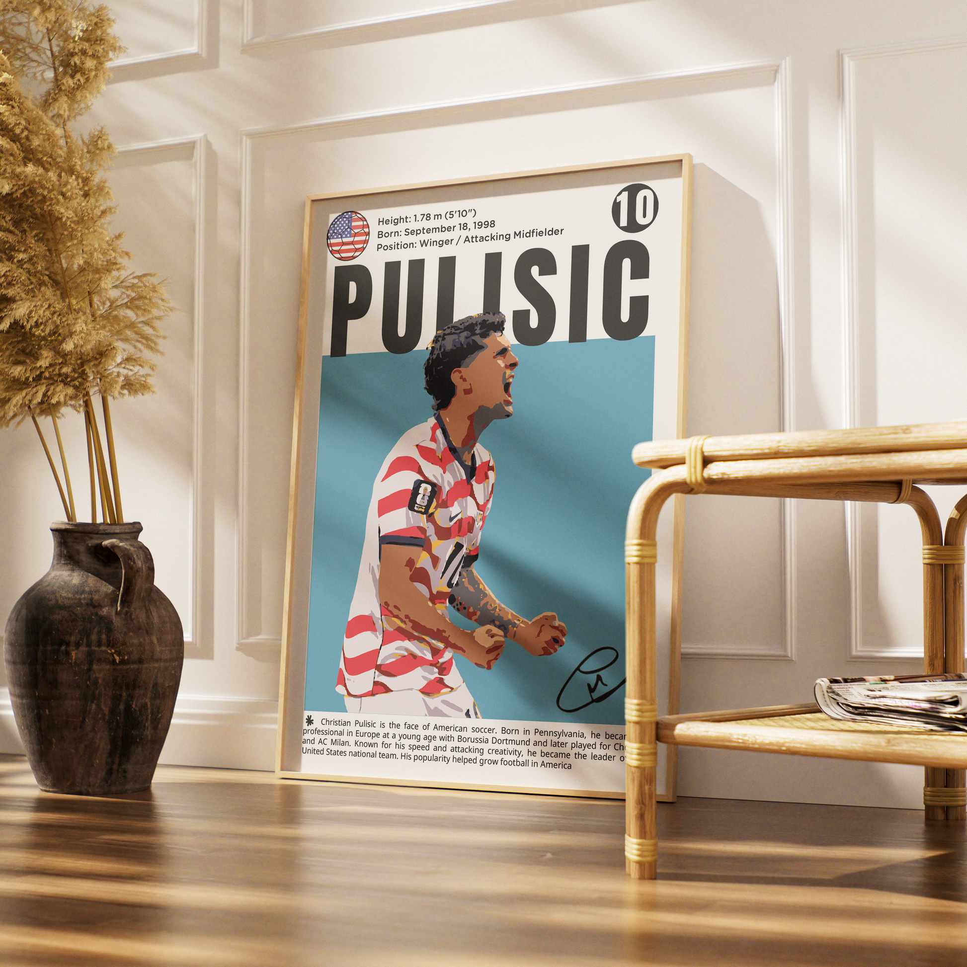 A framed poster of soccer player Paul Escobar, signed with a black marker, leaning against a white paneled wall on a wooden floor next to a rattan side table and a vase of dried grass.