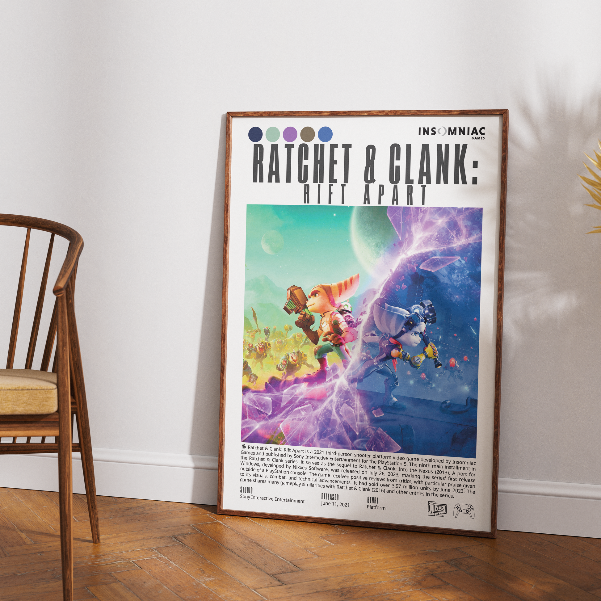 A framed poster leaning against a white wall on a wood floor, showing colorful sci-fi artwork with the title 'Ratchet & Clank: Rift Apart' and the Insomniac logo. A wooden chair is partially visible on the left.