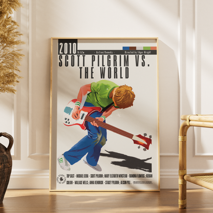 A framed poster print leaning against a white paneled wall on a wooden floor, showing an illustrated scene of Scott Pilgrim playing an electric bass guitar with the text '2010 Scott Pilgrim vs. The World.
